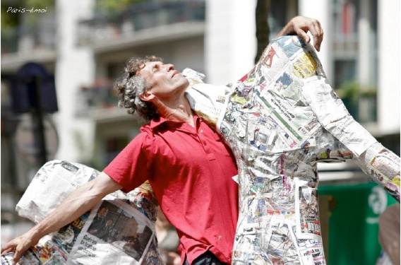 Marc Planceon en chemise rouge, entouré de papier journal, avec la Cie Mi-Octobre